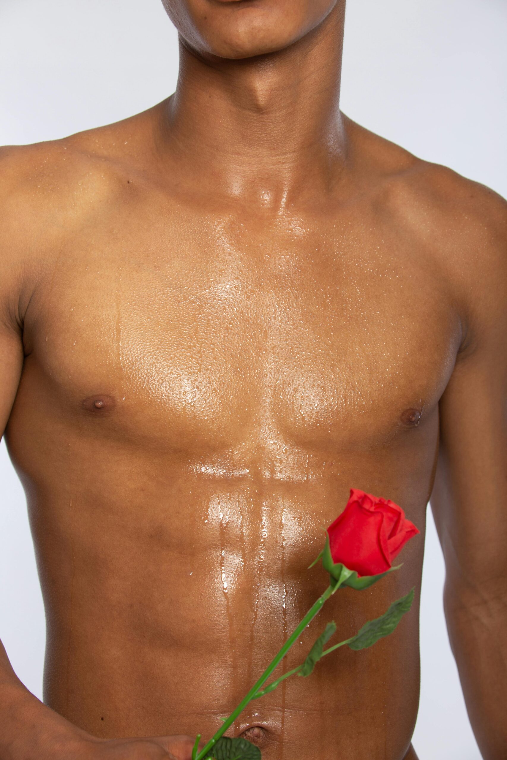 Close-up of a glistening torso holding a red rose, symbolizing passion and strength.